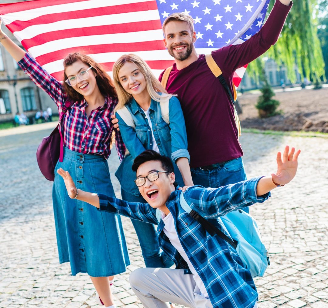 smiling multicultural students with american flag in park